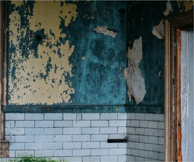 An old, dilapidated building with peeling paint, a door, and a crumbling wall.