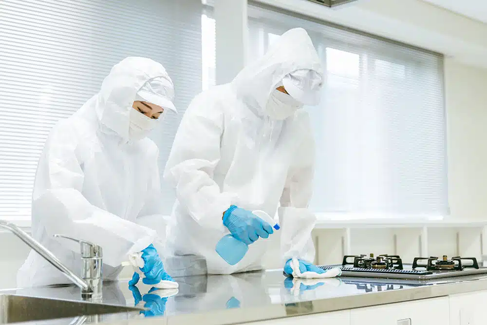 Two individuals in white protective gear cleaning a kitchen.