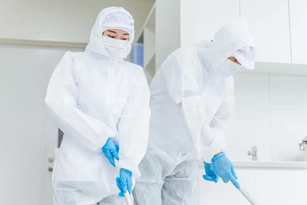 Two individuals in white protective gear cleaning a kitchen.