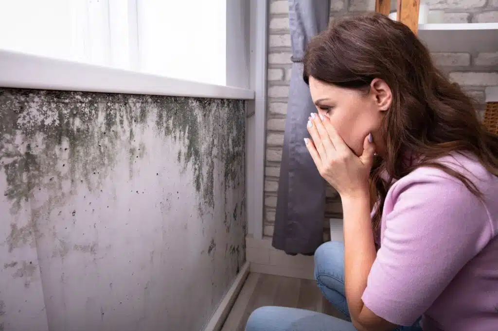 Female sitting on floor, hand covering face. Addressing long-term water damage effects