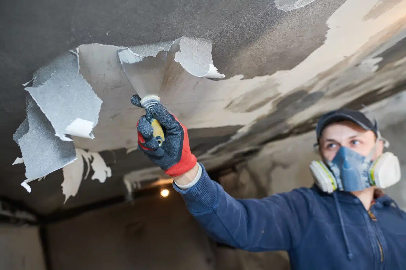 A man in a blue shirt and blue gloves painting a ceiling. Disaster restoration experts at work.