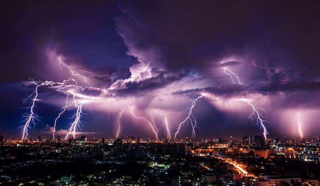 A city skyline at night with lightning bolts striking down, under a severe thunderstorm warning.